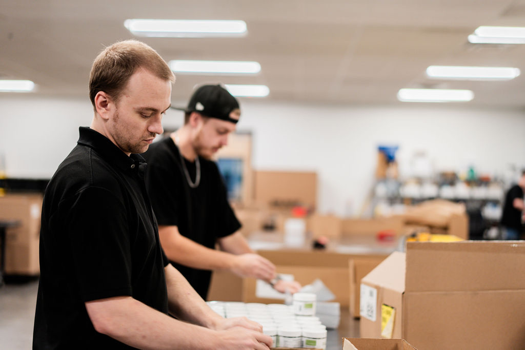 Two Uptime warehouse team members packing supplement orders into shipping boxes
